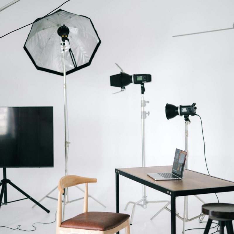 Wyposażenie Modern photography studio with lighting equipment and a laptop on a desk.